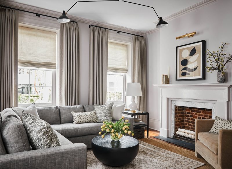 Yin & Yang: The light-filled living room features warm touches, from a neutral rug and pale gray drapes to a coffee-colored mohair chair from McGee & Co. The theme is balanced by a custom sofa covered in a gray performance fabric from Perennials and black accent pieces. The round “Maureen” coffee table, also from McGee & Co., allows for easier flow in the compact space.