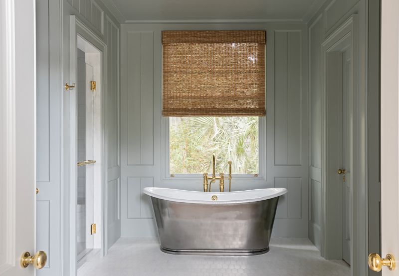 A freestanding cast iron tub from Waterworks with brass fixtures from Bird Hardware is a centerpiece in the panelled room painted in Farrow & Ball “Light Blue.”
