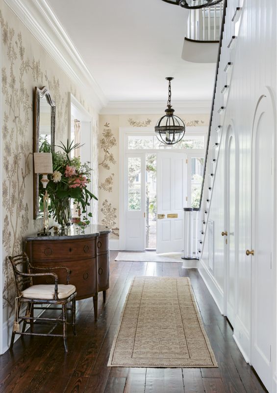 HAUTE ARRIVAL: The entrance hall adds a dash of drama courtesy of exquisite Gracie “Parchment Vista” wallpaper. Shades of cream together with gilt and silver produce a mesmerizing effect, complemented by the curves and scale of a circa-1850 stone-topped Italian buffet from Foxglove Antiques. Two English Regency armchairs from Charleston’s Golden & Associates Antiques round out an eclectic mix of European pieces.