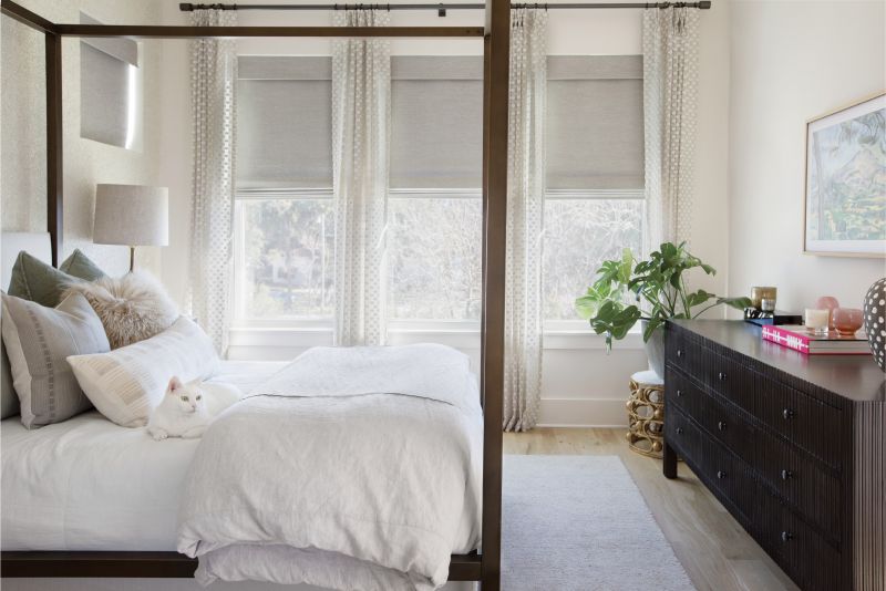 NATURAL INSTINCTS: Calming hues in the master bedroom draw from the palette of oaks and marsh just beyond the windows. A brass Mitchell Gold + Bob Williams canopy bed and long, low dresser provide depth, while Ellis Dunn “Michelle Fog” drapes and Phillip Jeffries “Africana” seagrass wallpaper add texture to the scene.