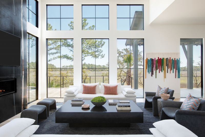 YIN & YANG: Erickson helped her clients move from a more transitional style in their previous home to the bold look they were craving. She pulled the Sherwin Williams “Iron Ore” paint from the exterior into the main living space, anchoring it with a striking book-matched, honed Nero Dorato marble fireplace surround. Dark furniture—Verellen chairs in a bouclé fabric and a wood coffee table designed by Erickson—are balanced by soft white sofas and walls painted with Benjamin Moore’s “Decorator’s White.” The designer also pulled hues from the marble and tied them into custom art pieces that pop from the neutral backdrop.
