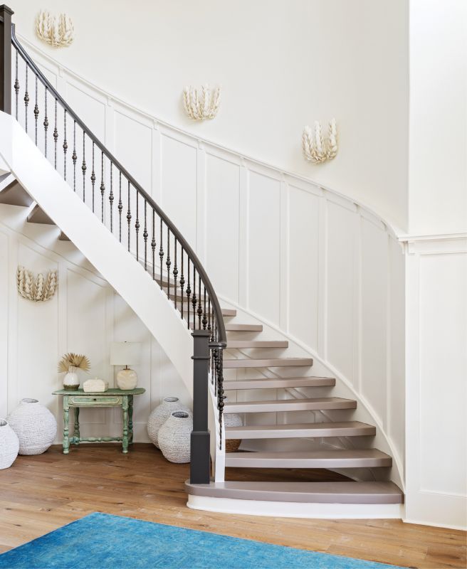 WELCOME IN: “It was a beautiful canvas to work with,” says interior designer Allison Elebash of the Leonard home, adding that its bones—including the foyer’s custom millwork and sweeping floating staircase—needed only cosmetic updates. She painted stair treads Farrow & Ball’s “Charleston Charm” and installed white oak floors throughout the house to hide sand and fur. An azure rug from Antiques of South Windermere, seafoam-painted table from Acquisitions Interiors, woven jugs from GDC Home, and Palecek “Coco Magnolia” sconces (fashioned from hand-cut coconut shells) ground the space in its coastal locale.