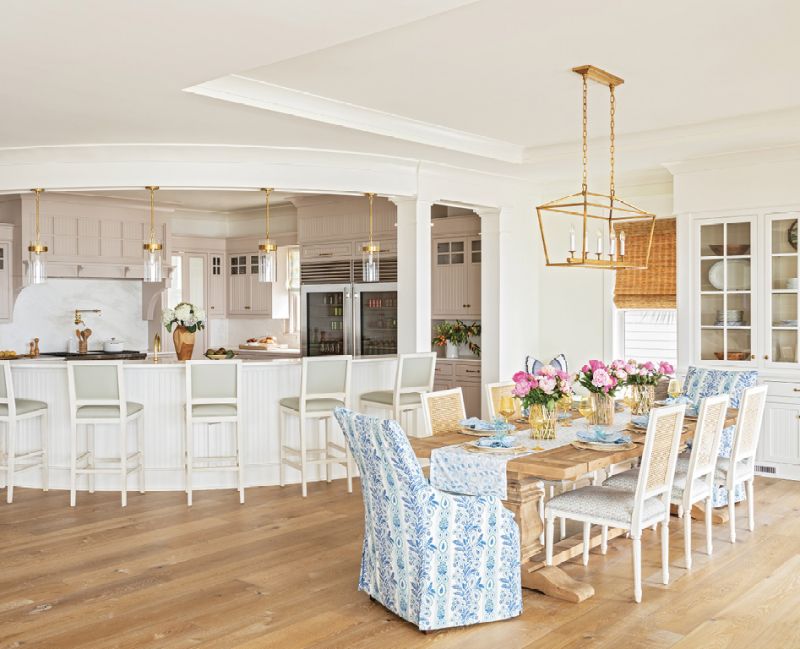 GATHER ROUND: The curved, two-tier kitchen island, original to the home, is a high-traffic area, for the boys especially. “I like to see them all lined up there just like when they were little,” says Amy, noting they had a similar island decades ago. Formerly a mix of white and dark wood, the kitchen cabinets now wear Farrow & Ball’s “Elephant’s Breath,” with a hint of pink. “It’s so beautiful when you get that sunset light coming in,” says Allison. Glass and brass pendants from Circa Lighting add further warmth to the space.