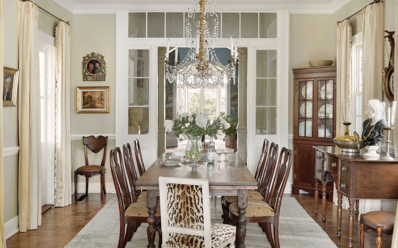 Fine Dining: The rotunda opens into the dining room, a later addition, which itself leads to the renovated kitchen. Ralph opened up these rooms to create one continuous space. She kept the original basket-weave parquet floors, continuing them into the kitchen to tie the rooms together. She also updated the window trim work to better match the original architectural details and added an ornate chandelier from David Skinner Antiques above the dining table. The antique sideboard holds two urn lamps from Wynsum Antiques & Interiors; a Grecian figure below a convex mirror from Well Furnished adds a touch of whimsy to the scene.