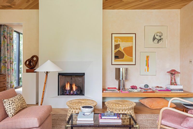 A stucco fireplace and cypress floating bench pair with the pale peach Venetian plaster walls to create continuous clean lines throughout the home. Hranowsky filled the space with treasures collected on her travels, including handwoven tule fiber stools from Mexico City, a “Shroom” lamp by Matthias Vriens, and a vintage chrome lamp found during a trip to Madrid. “I think homes are most interesting when they feel collected and traveled and tell a personal story of their inhabitants,” she says. White oak planks on the floors and ceiling run in different angles to delineate the kitchen and the living room. The handmade Italian rattan armchair from Bonacina picks up the pattern in the drop cloth curtains, which Hranowsky designed and had painted by local artist Beth Williams.