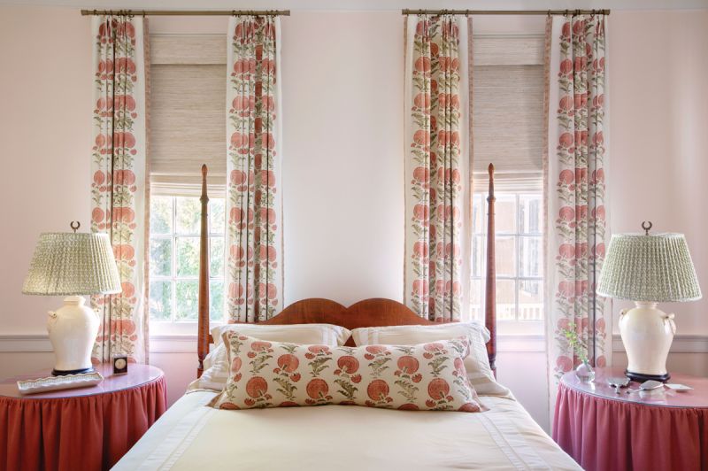Pretty in Pink: Upstairs, the Jasper “Indian Flower” hemp fabric, used for the drapes, bed skirt, and pillow, provides interest in the primary bedroom. Antiques fill out the room, from the tiger maple four-poster bed and Great Windsor Chair Company lamps with Fermoie shades to the dresser topped by tea caddy lamps.
