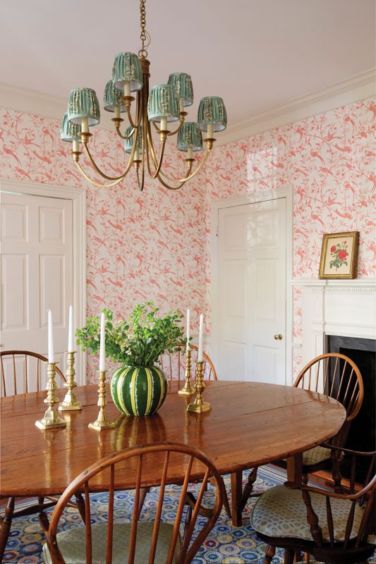 Rosy Outlook: The Brunschwig & Fils “Bengali Rose” wallpaper sets the tone for the colorful dining room, where antique Windsor chairs surround a large farm table Caitlin sourced in California.  Pattern is infused throughout the room and into the adjoining kitchen, from the Chelsea Textiles plaid seat cushions to the Jasper “Gretta” fabric shades adorning the Visual Comfort chandelier.