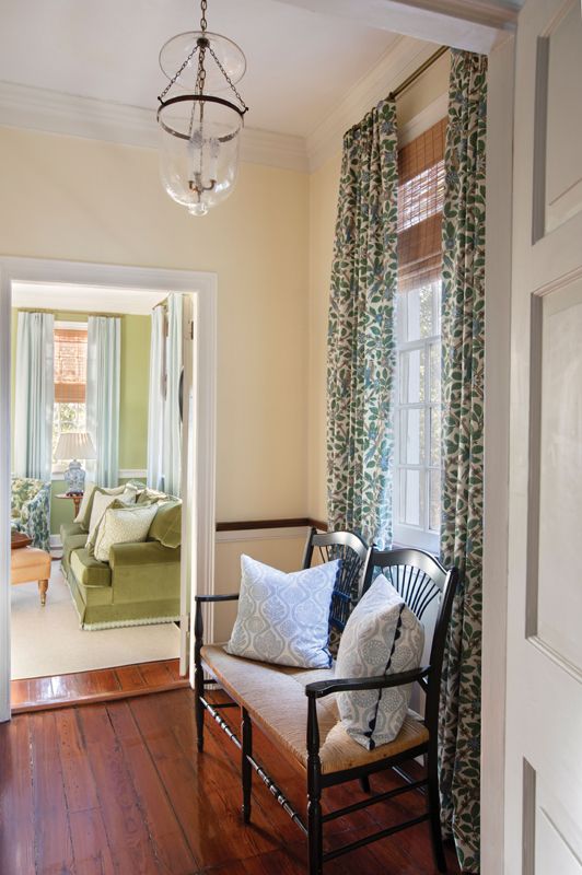 Pale blue drapes paired with a Halsey + Spruce velvet sofa and armchairs upholstered in Jasper “Grace” fabric highlight the leafy view beyond. In the hallway, GP & J Baker “Bamboo Bird” drapes and an antique bench provide a focal point.