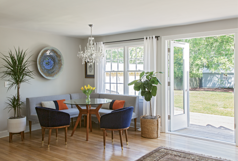 GATHER ’ROUND: Up to seven people can fit comfortably in the West Elm-clad dining nook. When hosting a large group, Rachel simply swaps this glass tabletop out for a larger version. Pottery Barn drapes, a chandelier from Carolina Lanterns & Lighting, plants from Hyams, and a bowl hand-thrown by Louisiana artist Craig McMillan finish off the space.