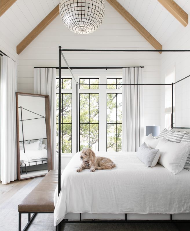 Simply Luxe: The paired-down master suite feels glamorous yet comfortable. Tying into the black steel of the windows, the iron-framed “Marco Bed” by Oly Studio is softened by plush Peacock Alley bedding and a worn leather bench atop a vintage Oushak rug. A Restoration Hardware chandelier and Room & Board mirror complete the space.