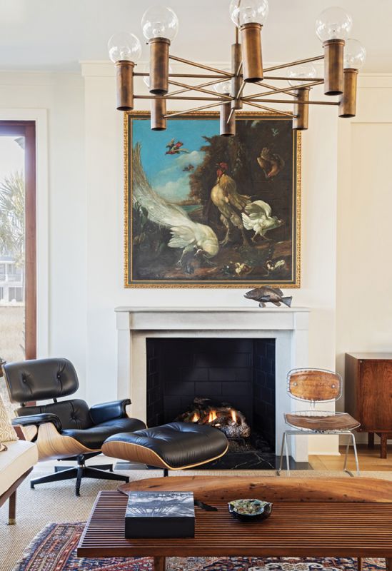 Lounge Act: A 17th-century oil painting in the manner of English painter Marmaduke Cradock adds a touch of drama above the fireplace while tying in the blue sky theme. A classic Herman Miller Eames chair and ottoman in black leather and mid-century George Nelson-style slatted coffee table are watched over by a 1960s patinaed metal chandelier.