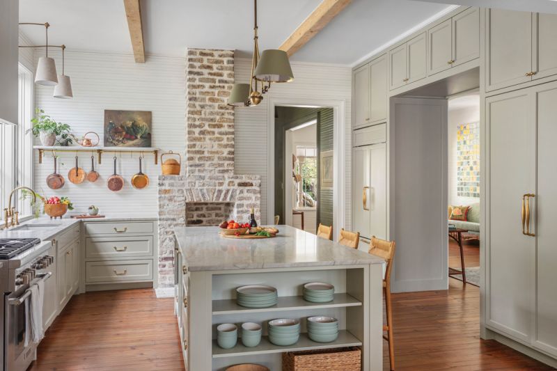 The fireplace backs into the kitchen, where the exposed brick chimney provides warmth and a unique architectural element. Cabinets painted in Farrow & Ball “French Gray” complement the “Wimborne White“ walls.