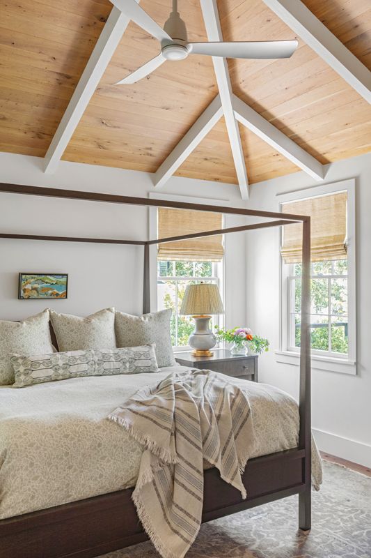 Vaulted ceilings are repeated in the primary bedroom suite, where white pine paneling and a four poster bed from Crate & Barrel complete a simple but sophisticated space.