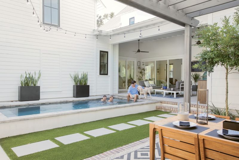 Fun Zone: Three sliding glass doorways open to the outdoor entertaining areas, including a lounge space with aluminum and teak love seats from AllModern and a woven lantern from Lyndon Leigh, Cristian’s “kitchen,” a compact pool where the boys and goldendoodle Kylie splash and play, and the pergola-covered dining area with a teak table and chairs.