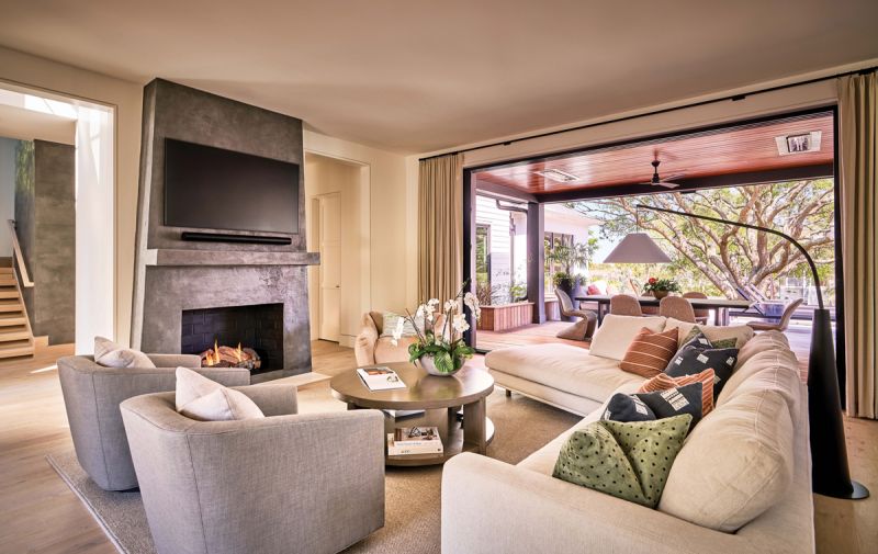 Curves & Contrasts: An asymmetrical sofa in the main living space keeps the room open and allows for an easy flow. The plaster fireplace by Jess Kolar Artistic Designs contrasts beautifully with creamy walls; the reglet reveal in place of crown molding continues the clean, modern lines of the home. These contemporary elements are softened subtly by comfy chairs in soft colors from Restoration Hardware and Maiden Home.