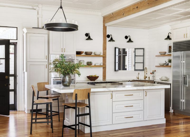 Exposed wood beams and floating wooden shelves are accented by counter stools from Muuto. The black-metal theme continues in the Ralph Lauren chandelier and Original BTC Lighting wall sconces.