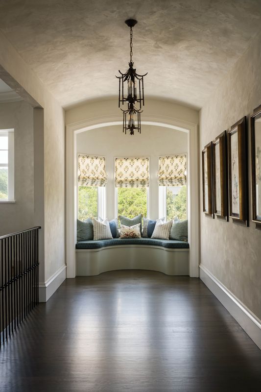 A curved window seat at the end of the gallery hall is upholstered with a Cowtan & Tout fabric with pillows in textiles by Katie Leede & Company, Rose Tarlow, and McLaurin & Piercy.