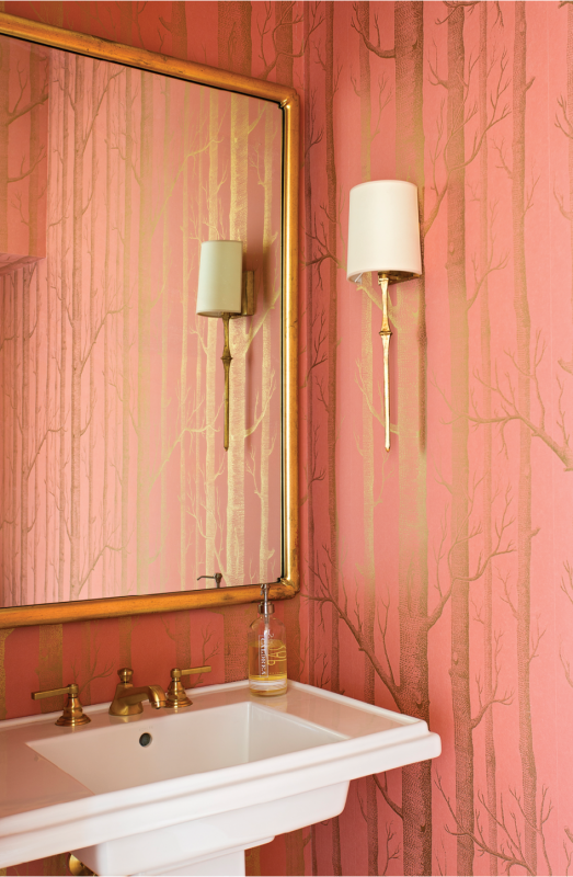 The powder room dazzles in radiant gold-flecked Cole & Son wallpaper, accented by a mirror found at John Pope Antiques and delicate sconces from Circa Lighting.