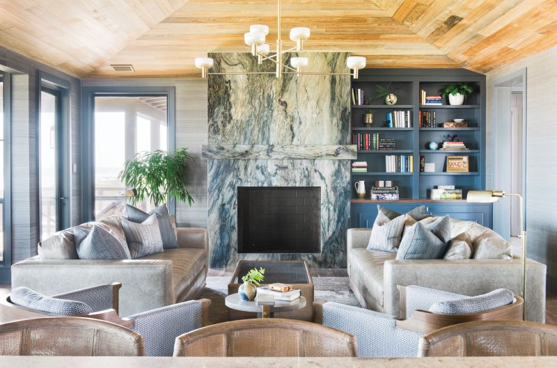 With the Tide: Situated on the top floor, the main living space is dominated by a fireplace set in “Blue Tides” granite from AGM Imports. Horsehair grasscloth wallpaper in “Clydesdale” by Phillip Jeffries continues the textural feel evoked by the stone’s veining. Leather sofas from Verellen and Osborne & Little fabric-clad club chairs by Holly Hunt lend warmth and comfort to the scene, illuminated by Cartwright New York’s hand-brushed brass “Otto Luce” chandelier.