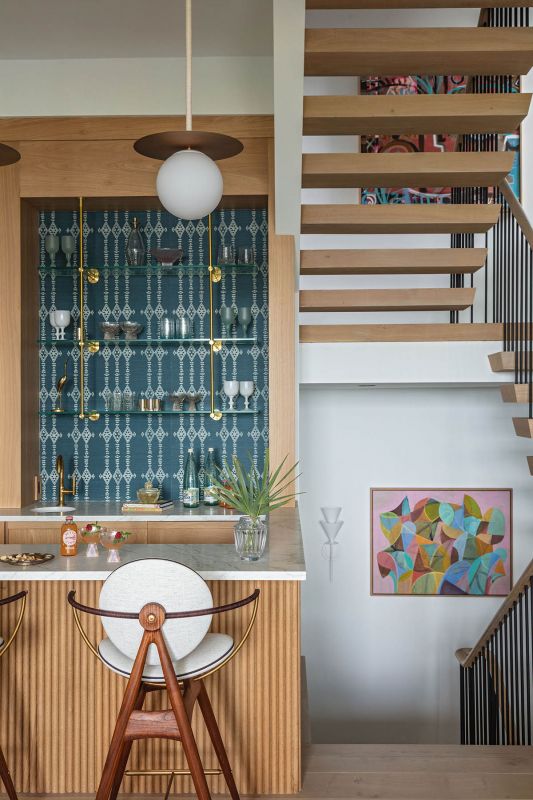 Brass and glass shelving in the bar highlight the geometric “Berber” wallpaper by Peter Dunham Textiles.