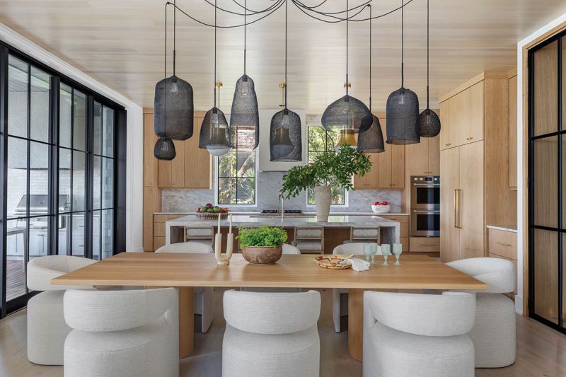 A cluster of nine “Kute” pendants from Atmosphere D’Ailleurs drifts above a custom white oak table, paired with sculptural A. Rudin chairs. Beyond, a marble-topped island anchors the kitchen beneath a hand-troweled plaster hood and Visual Comfort “Precision” pendants.