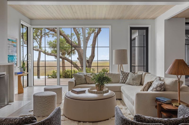 Walls of glass frame the view from the living room, which features a Verellen “Gregoire” sectional and swivel chairs arranged around the reeded marble fireplace. Washed poplar on the ceiling adds warmth.