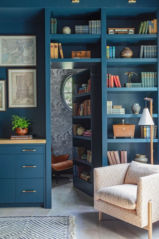 A pivoting bookshelf opens into a secret reading nook where a Keeks Design lounge chair and ottoman face floor-to-ceiling shelves of antique books.