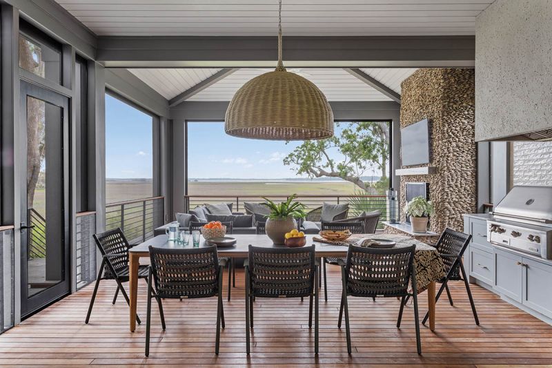 The screened porch is an extension of the main living space, with a Palecek “Wisteria” chandelier suspended above an Urbanspace Interiors dining table and Janus Et Cie “Anatra” armchairs. A hand-stacked oyster shell fireplace anchors the room.