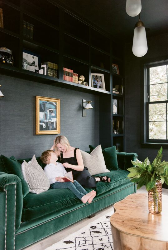 Molly and Sawyer read in the library, where the Phillip Jeffries “Manila Hemp” wallpaper in “charcoal” and Hickory Chair sofa upholstered in emerald-green velvet by Ralph Lauren set a moody, masculine tone.