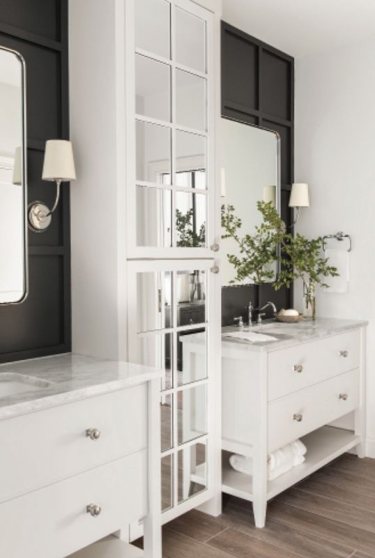 His & Hers: Two vanities in the newly created en-suite bath for the primary bedroom continue the home’s black-and-white theme. Vendome sconces with white shades peek out from the black paneled walls and honed Carrara marble countertops on custom designed vanities are topped by nickel faucets from Water Street Brass.