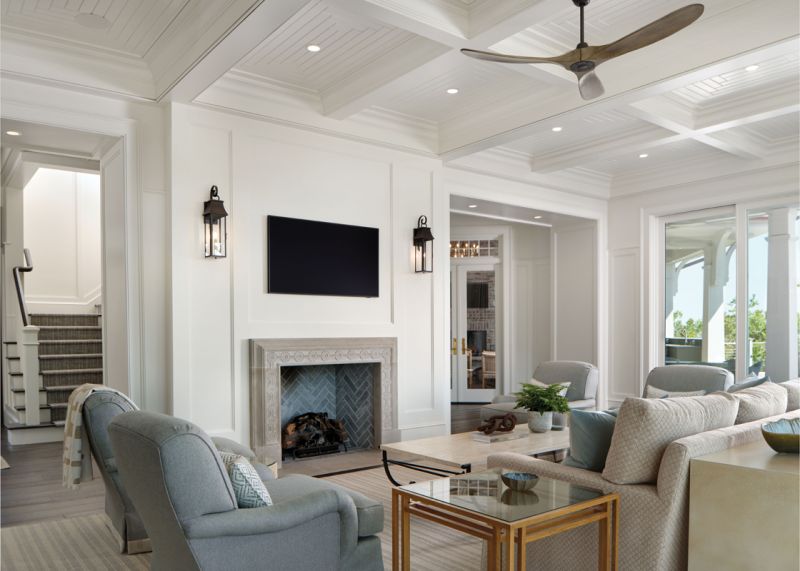 Large windows with decorative transoms combine with glass doors leading to the deck and pool to provide an expansive view of the surrounding marsh. Interior designer Caroline Willis selected warm neutrals for the living room so as not to compete with the beauty outside. Benjamin Moore “Swiss Coffee” walls and a light beige Schumacher fabric for the sofa complement the custom chairs covered in a soft blue Travis & Company fabric.