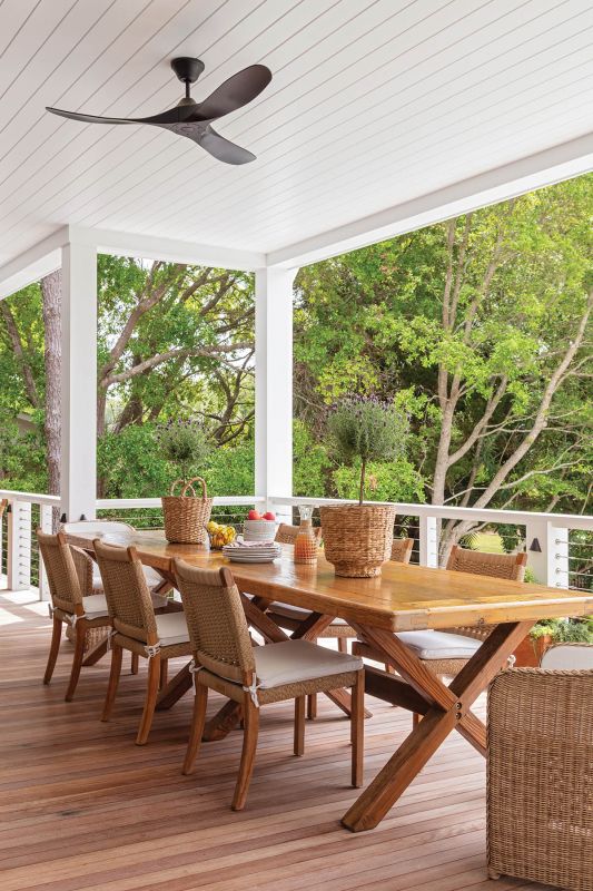 On the back porch, a teak table from Elizabeth Stuart Design sits beneath the beadboard ceiling, paired with woven chairs from GDC for catching the salt breeze.