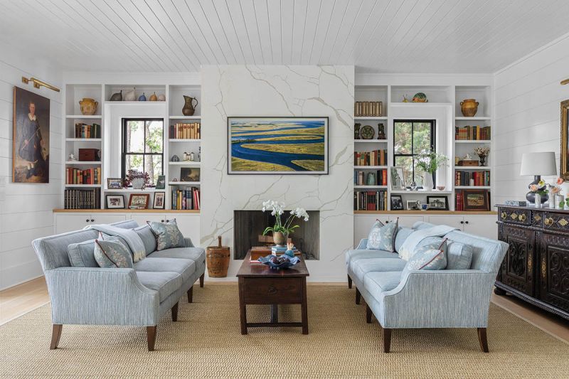Two Ferrell Mittman “Madison” sofas in Colefax and Fowler “Croft” fabric in “Old Blue” break up the dark wood of the room’s antiques. A marble fireplace surround and the Samsung Frame TV mixes in some modern.