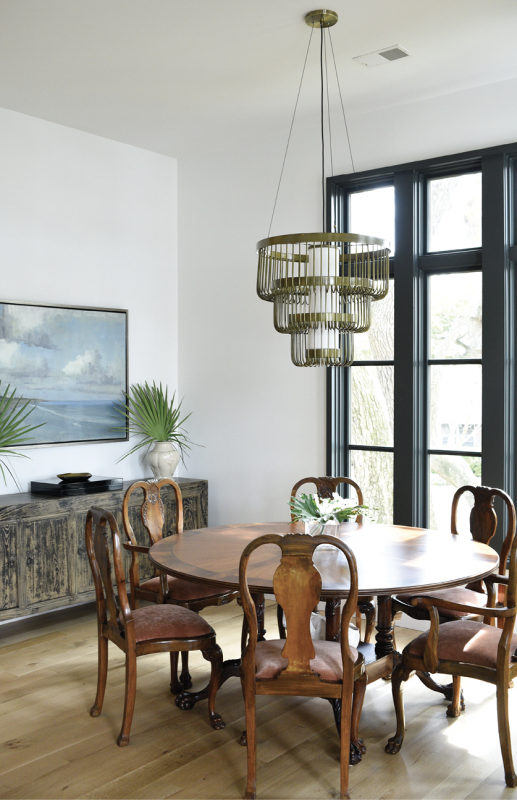 The dining room completes the open plan living area, providing floor-to-ceiling views of the treetops from the antique reproduction table and antique chairs. The distressed wood sideboard from ESD anchors a calming ocean vista by Georgia artist Kathy Cousart. A tiered, brushed-brass chandelier from CB2 completes the look.