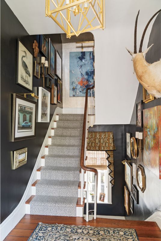 GALLERY SPACE:  A collection of artwork amassed over two-plus decades hangs in the stairwell. “There’s a piece of art floating around here that I paid $550 for when I was like 24, and that was more than my rent at the time,” he says, noting that, through Mitchell Hill, he has represented many of the artists whose works are on display. “There’s no one hanging on these walls that I don’t know—unless they’re dead.” The walls, painted in Farrow & Ball’s “Pitch Black,” and the Stark “Fowler Stria” carpet runner provide a neutral counter to the art.