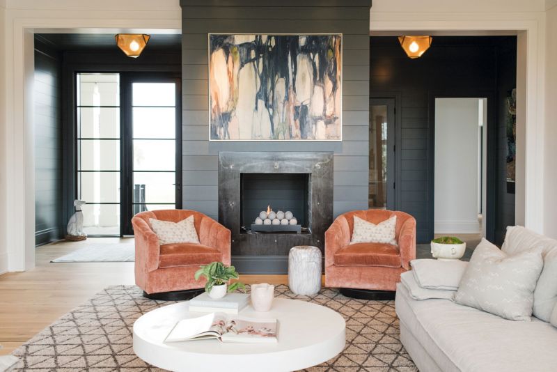 The moody hues of the foyer—shiplap painted in Farrow & Ball “Down Pipe”—continue into the living room around the dramatic fireplace. Crushed velvet chairs and an abstract painting by Jill Pumpelly add depth to the otherwise neutral palette.