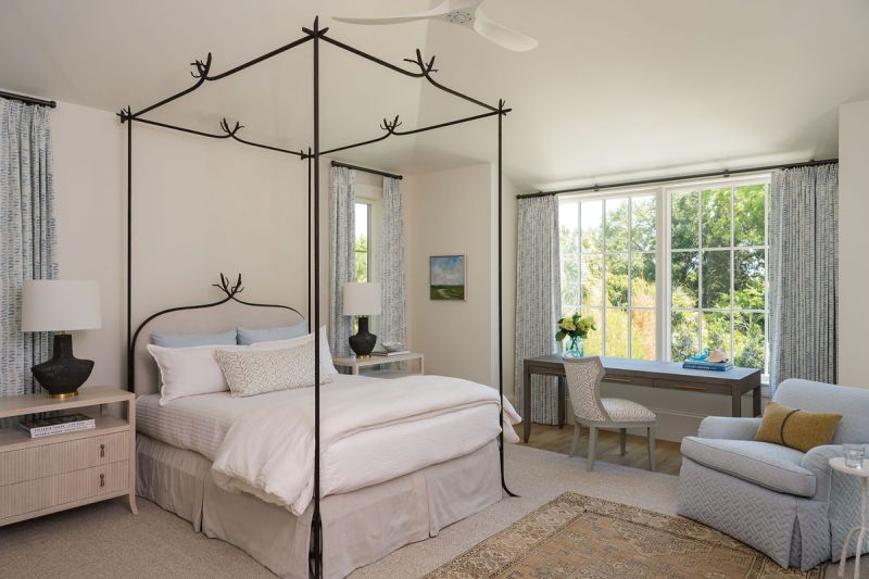 Into the Woods: Located on the main floor, the primary suite enjoys a lush view of the surrounding maritime forest, a fitting backdrop for the “Twig” iron bed by Formations that was originally in the couple’s mountain home. Designers Means & Carney softened the look with floral fabrics, including pretty blue drapes by Savannah Hayes.