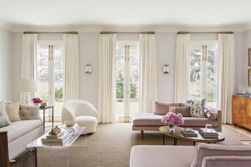 La Vie En Rose: Natural light spills into the living room through French doors, framed by custom drapes in a Joseph Noble fabric. The soothing palette, anchored by walls in Farrow & Ball “Blackened,” is complemented by pops of pink from two West Elm chaises re-covered in Kravat velvet.