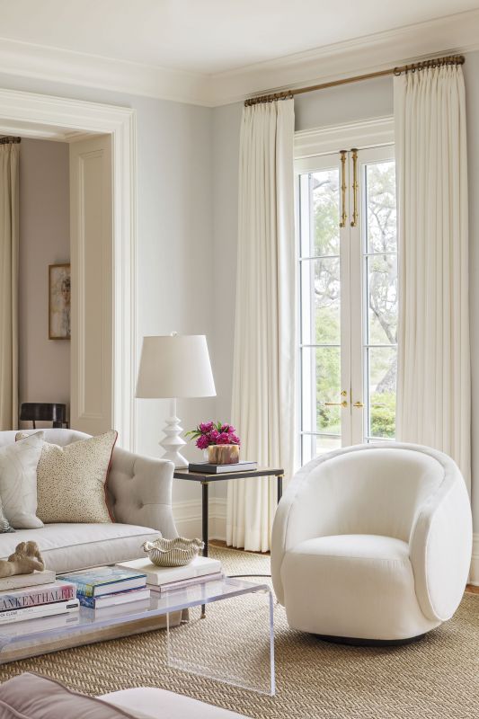 FORM & FUNCTION: The elegant curves of the Kravet swivel chair and antique sofa—upholstered in Perennials fabric with Samuel & Sons trim—contrast with the strong lines of the dark wood Arteriors end table, topped by a sculptural Villa & House lamp.