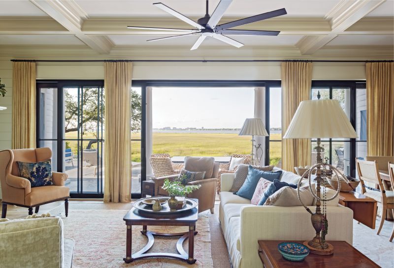 MARSH MOMENT: A wall of glass ushers panoramic views of the Ashley River and the peninsula into the large, open-plan living and dining room. Inside, a mix of modern and antique furnishings, including vintage hookah lamps and a Baker coffee table, carry through the marsh-inspired color scheme of amber and honey with highlights of ocean blue.