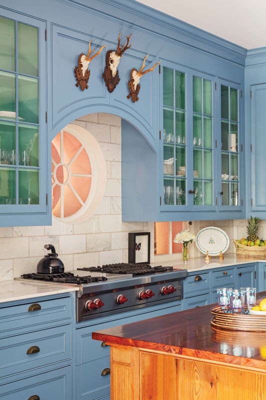 True Blue: The kitchen, which connects the entry hall to the garden room, is the heart of the home literally and figuratively. Cabinets washed in a soft blue feel warm and inviting next to wood accents from the original oak floors, wood mantel, and the refinished cypress plank island. A vintage Hermès scarf framed above the mantelpiece adds a fun contrast.