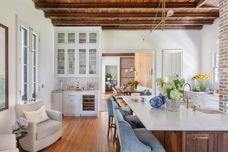 A marble-topped walnut island, lined with Charles Stewart “Mystic” counter stools in Schumacher “Cadet” velvet, centers the kitchen beneath a custom Riloh brass pendant light.