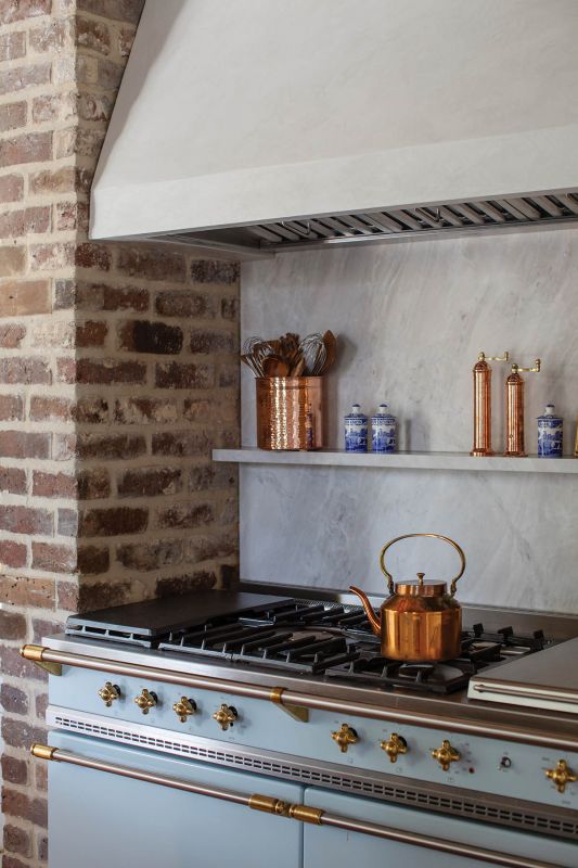 A blue Lacanche range fits into an original masonry fireplace beneath a hood by Charleston Plaster Co.