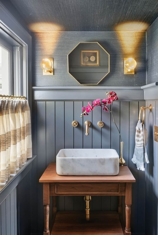 The entry hall powder room pairs York Wallcoverings “Gunmetal” grasscloth with Benjamin Moore “Amber Slate” trim. Riloh orb sconces and a Villa & House mirror sit atop a Split Woodworks walnut vanity and marble sink.