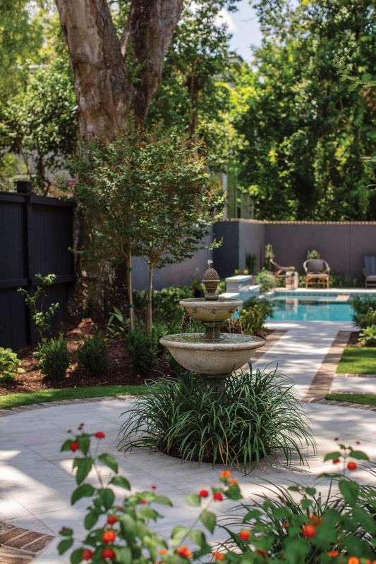 The home’s formal gardens, fully restored by Landplan Associates, now feature a tiered fountain and brick-edged pathways that lead to a new pool. The fence, painted in Benjamin Moore “Mopboard Black,” provides a neutral backdrop.