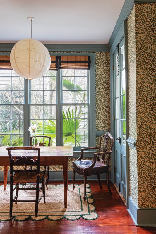 Garden View: A breakfast nook off the kitchen echoes the William Morris “Willow Boughs” wallpaper from the parlor, here offering green tones that complement the courtyard garden outside. An Akari rice paper lantern hangs above a well-worn, Southern pine kitchen table, accompanied by hand-painted, 19th-century Sheraton chairs and armchairs.