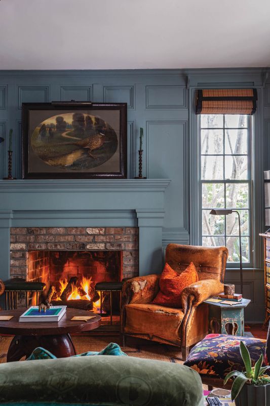 Cozy Elegance: Pillows wrapped in a burnt orange “Brer Rabbit” linen from Morris & Co. sink into leather French club chairs on either side of the fireplace. Facing an overstuffed antique love seat, the arrangement creates a shabby-chic feel reminiscent of an English country house.