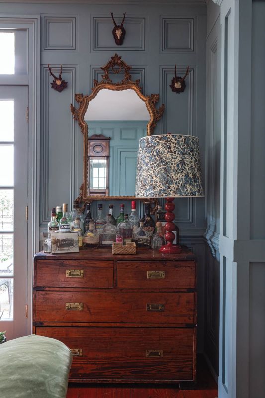 An English campaign chest serves as a bar, topped by a French rococo gilt mirror, surrounded by vintage Black Forest roe deer antlers.