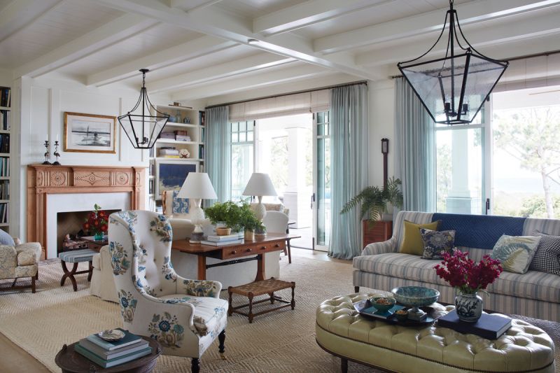 The light, bright interiors painted in “James White” by Farrow & Ball pull in hues from the picturesque view, including pops of green and blue and light-colored woods. A large sisal rug from Eve and Staron Studio anchors the space with comfortable furniture in pretty patterns and a green leather ottoman/coffee table by Nietert Antique Restoration.