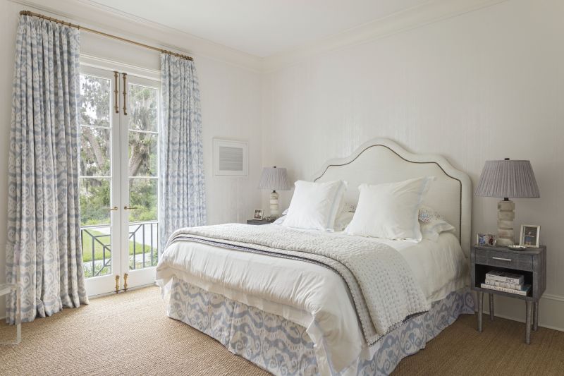 The primary bedroom is ensconced in floral drapes in Quadrille by Threadhouse, a Cowtan & Tout fabric-covered headboard, and Matouk bedding
